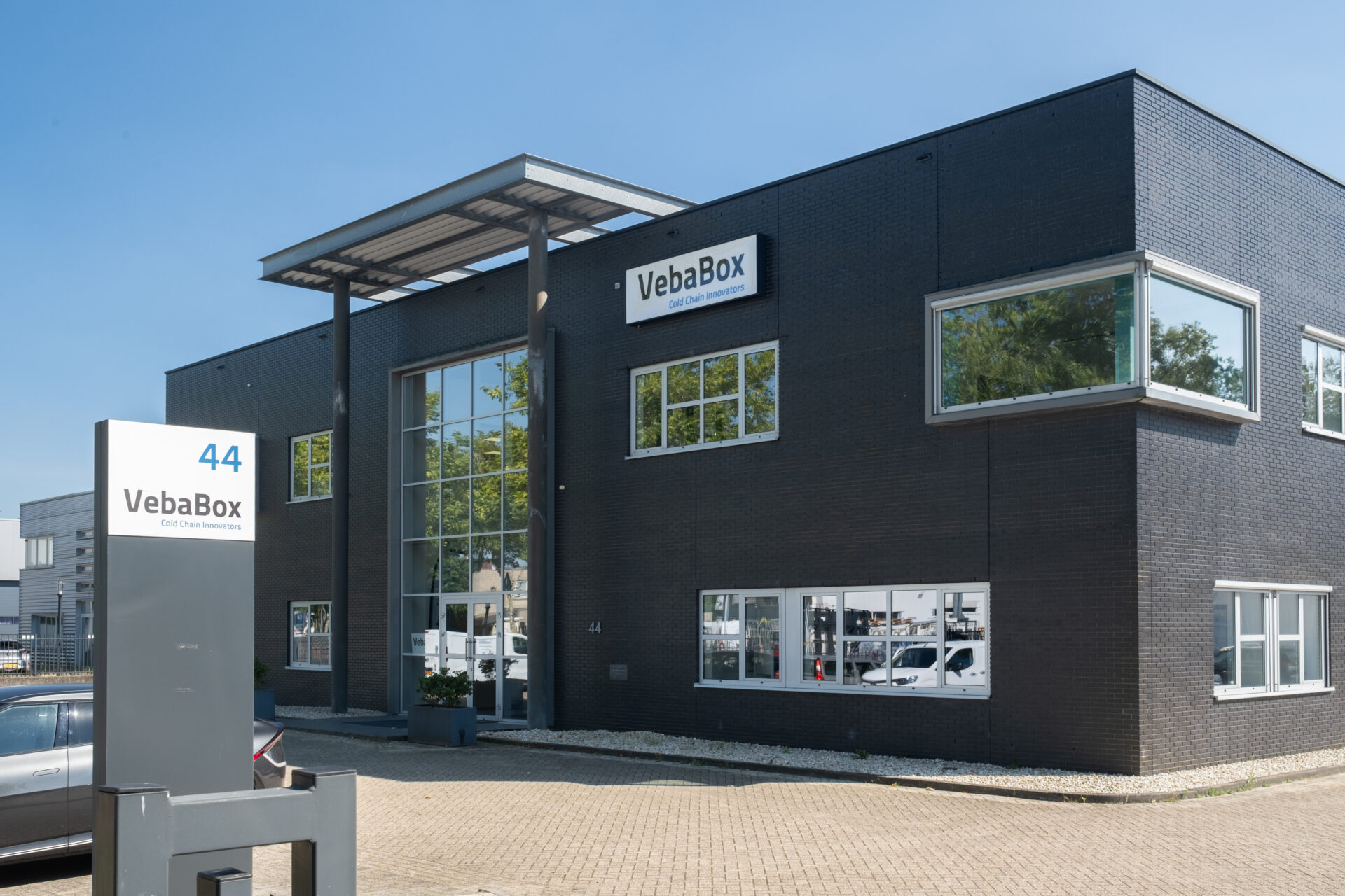Frontansicht des VebaBox-Hauptsitzes mit modernem schwarzen Gebäude, großem Logo am Eingang und reflektierender Glasfassade.
