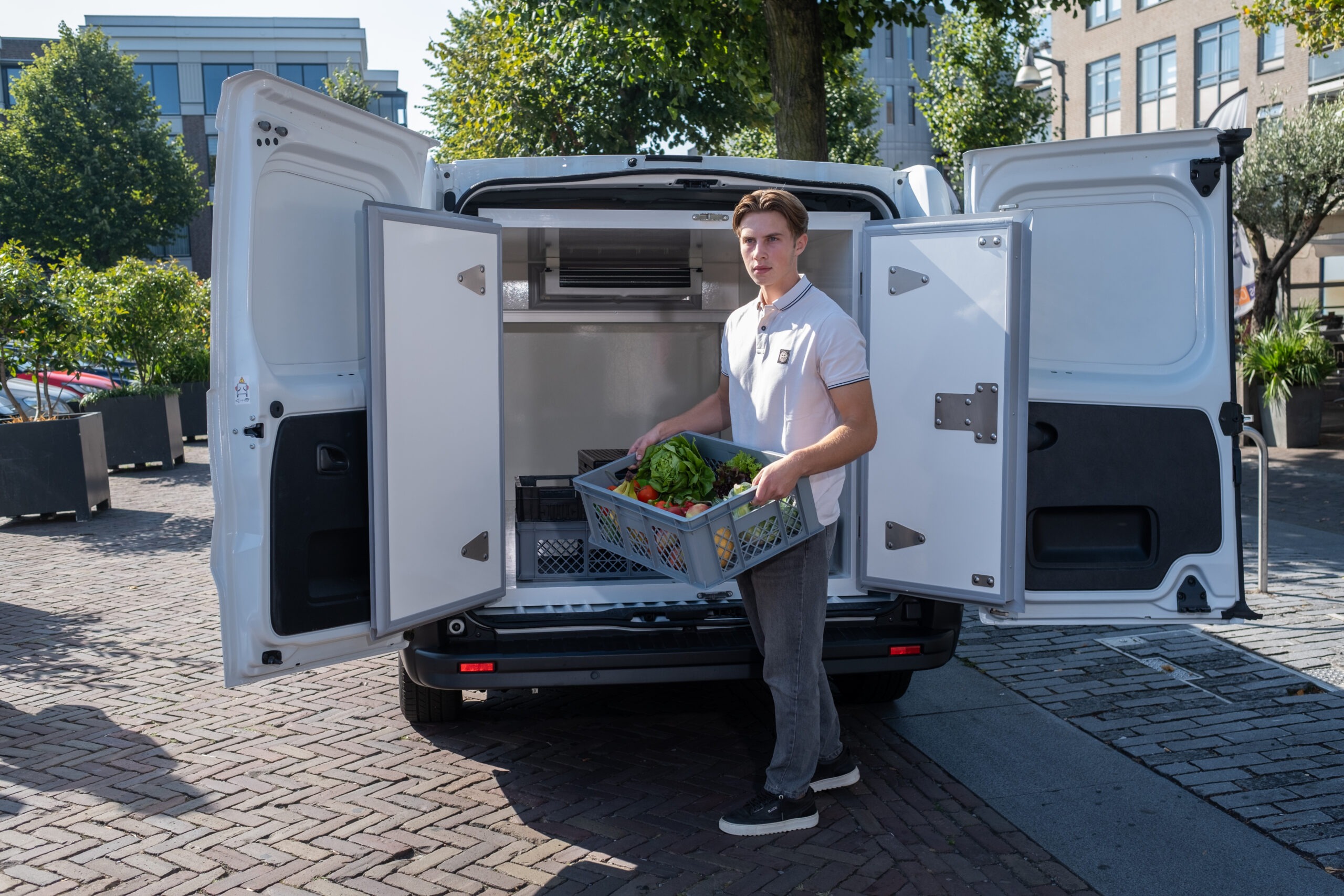 Ein Zusteller nimmt eine Kiste mit frischem Gemüse aus einer geöffneten VebaBox in einem Lieferwagen für die gekühlte Lieferung auf der letzten Meile.