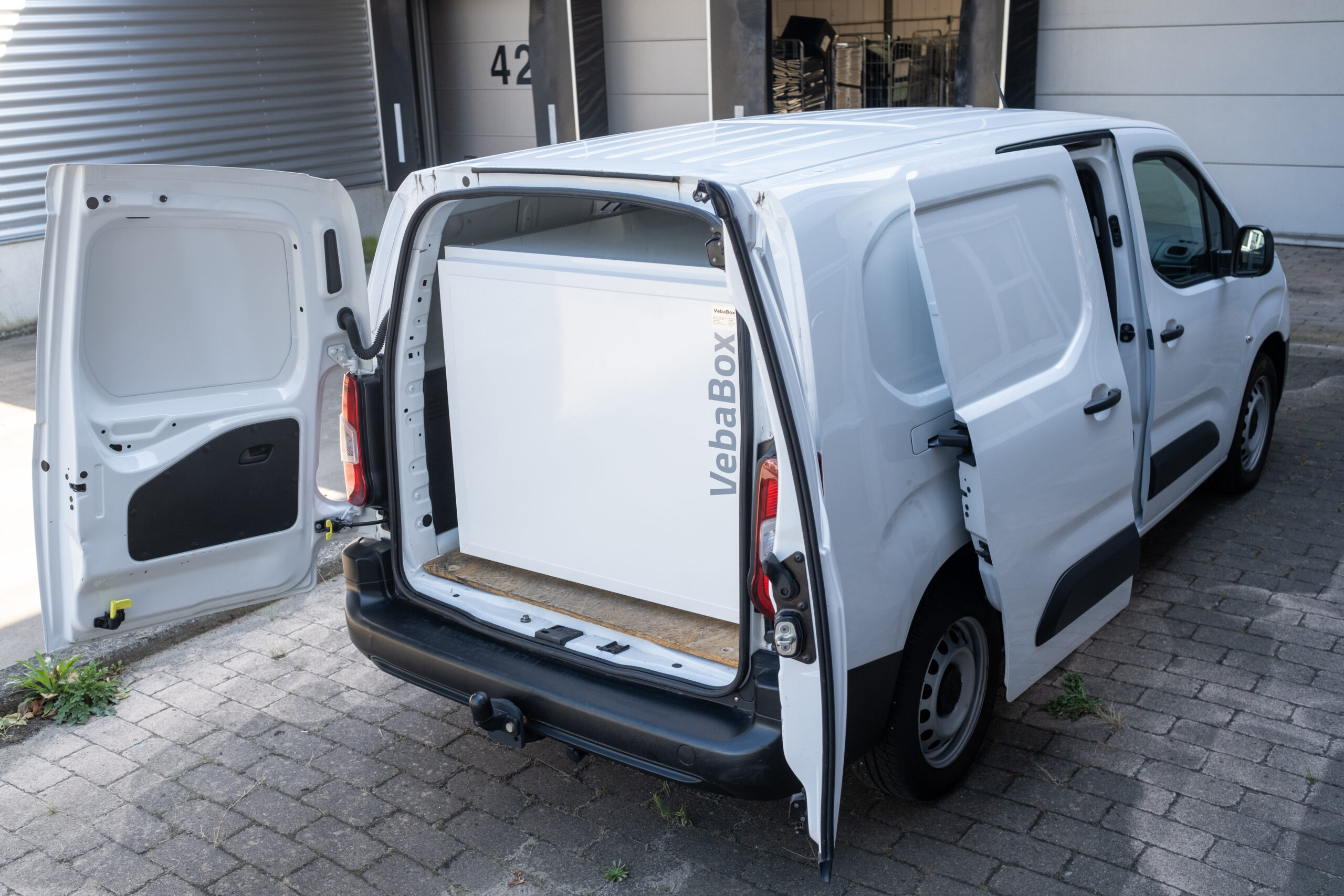Weißer Lieferwagen mit geöffneten Türen und integrierter VebaBox-Kühleinheit beim Beladen.